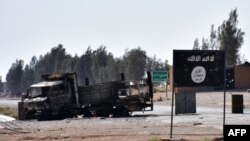 Izgorelo vozilo pored transparenta sa zastavom Islamske države u Siriji nakon ulaska sirijskih provladinih snaga u deo Rake, 11. juna 2017. 