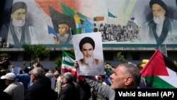 Iranians walk past a mural showing the late revolutionary founder Ayatollah Khomeini (right) Supreme Leader Ayatollah Ali Khamenei (left) and Basij paramilitary forces as they hold posters of Khomeini and Iranian and Palestinian flags in an anti-Israeli gathering after Friday Prayers in Tehran on April 19.