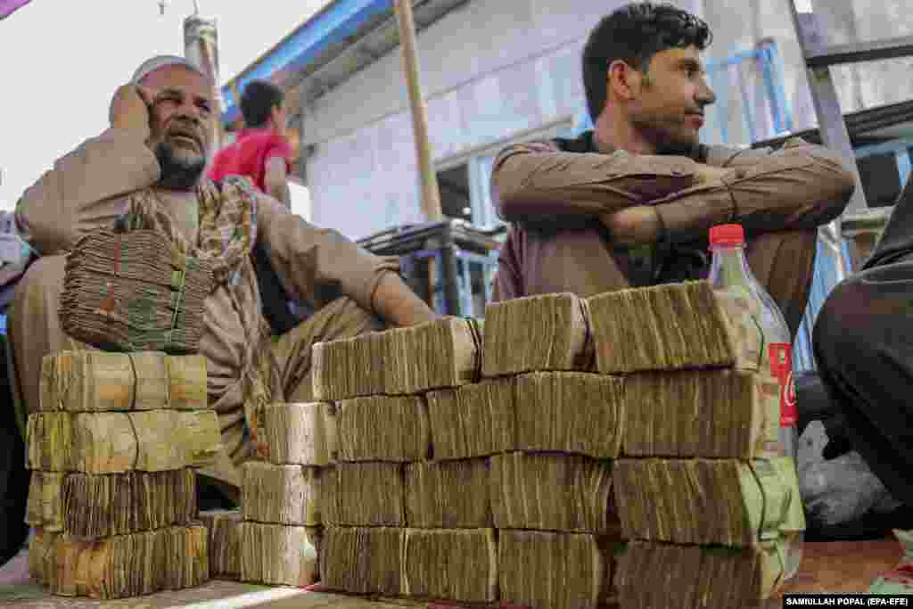 Afghan currency dealers sit by piles of old banknotes at a local market in Kabul.