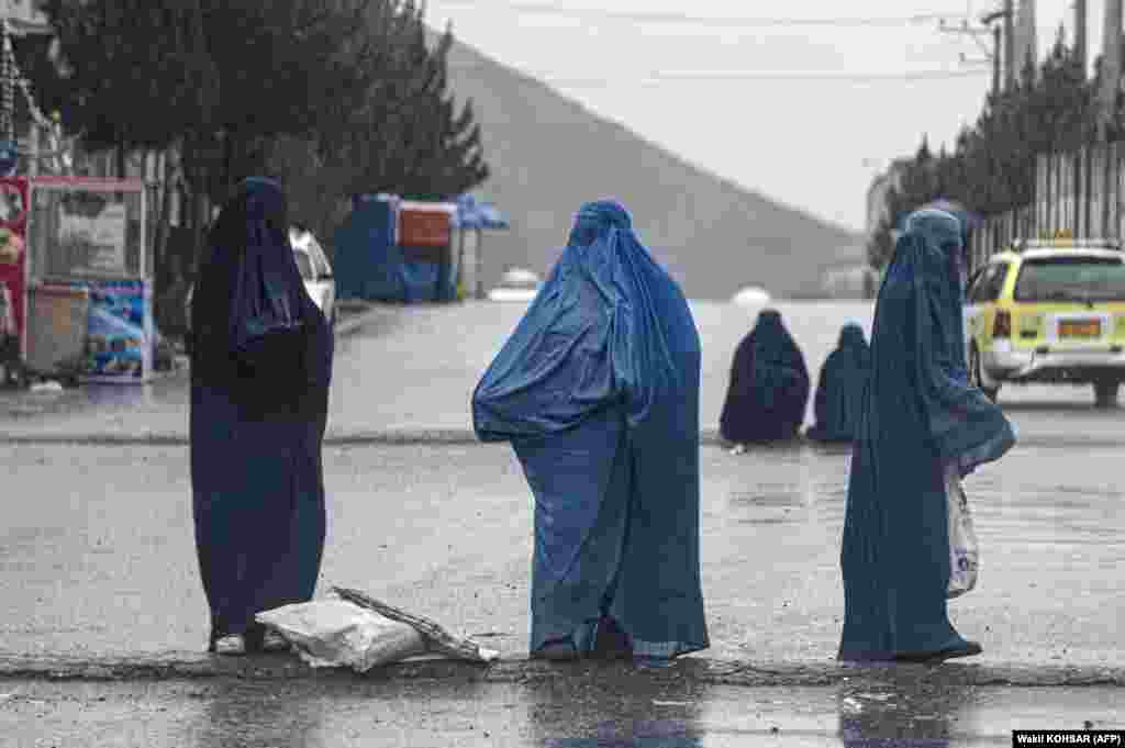 Afghan burqa-clad women beg for alms in the middle of a street during rainfall on the outskirts of Kabul on March 30.