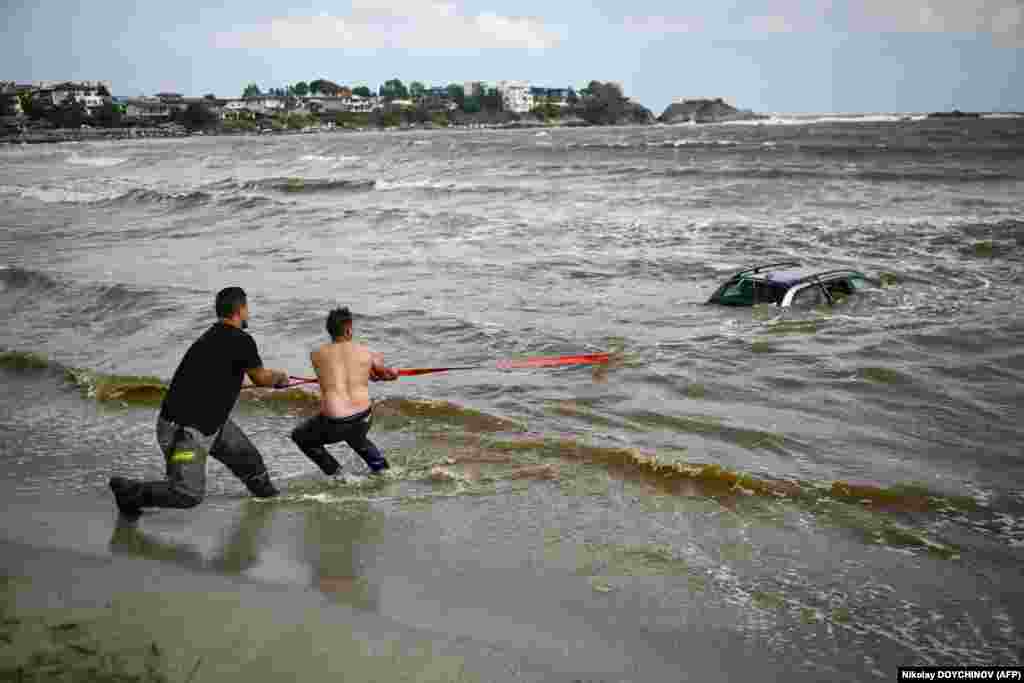 Oamenii încearcă să scoată o mașină scufundată în mare la campingul Arapia, lângă Tsarevo, de-a lungul coastei bulgare a Mării Negre, pe 6 septembrie 2023. Ploile abundente și furtunile de la sfârșitul zilei de 4 septembrie au făcut ca râurile să se reverse, distrugând poduri și ducând la evacuarea a peste 100 de turiști și localnici de pe litoral în locuri mai sigure. (AFP/Nikolay DOYCHINOV)