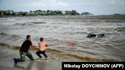 Două persoane încearcă să scoată afară o maşină cuprinsă de ape în zona campingulului Arapia din oraşul-staţiune Tsarevo, de pe coasta de sud a Mării Negre din Bulgaria.