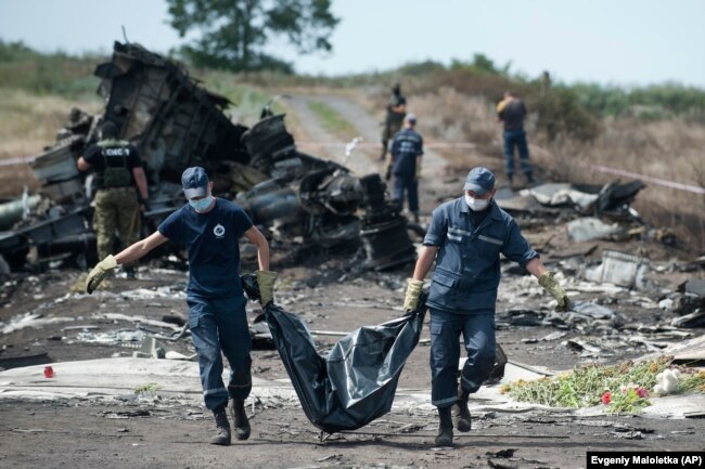 Українські рятувальники несуть тіло жертви в мішку для трупів, а проросійські бойовики охороняють місце падіння літака Малайзійських авіаліній рейсу MH17