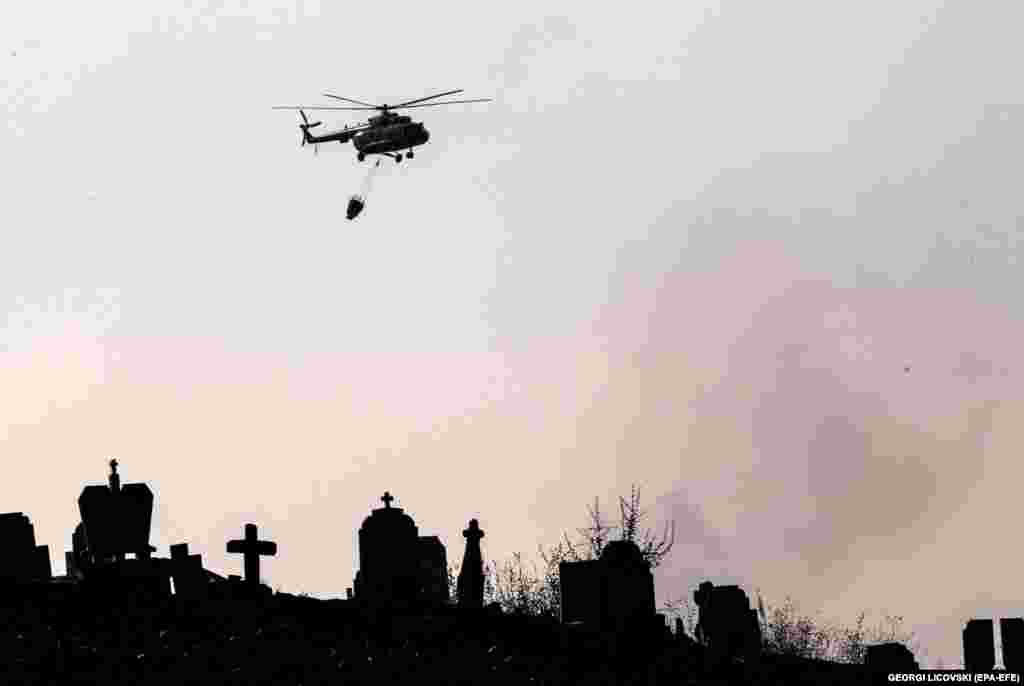 A firefighting helicopter flies over a cemetery near an area affected by wildfires in North Macedonia.&nbsp;