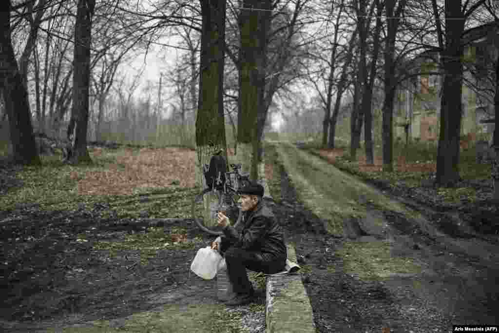 An elderly man smokes a cigarette as he waits to fill up jugs of water in Chasiv Yar near the front line in eastern Ukraine.