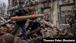Helyiek egy lebombázott bírósági épület mellett szednek tűzifát otthonuk fűtésére az ukrajnai Liman faluban 2023. december 14-én