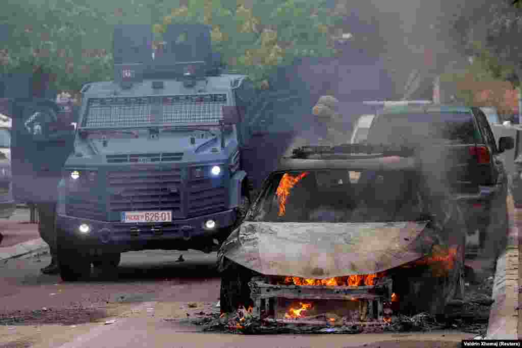 Pjesëtarët e forcave speciale të Policisë qëndrojnë pranë një makine të djegur, pas përleshjeve mes PK-së dhe protestuesve serbë në Zveçan. &nbsp;