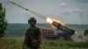 Український військовий на тлі вогню з системи «Град» по російських позиціях поблизу Бахмута, 21 червня 2023 року