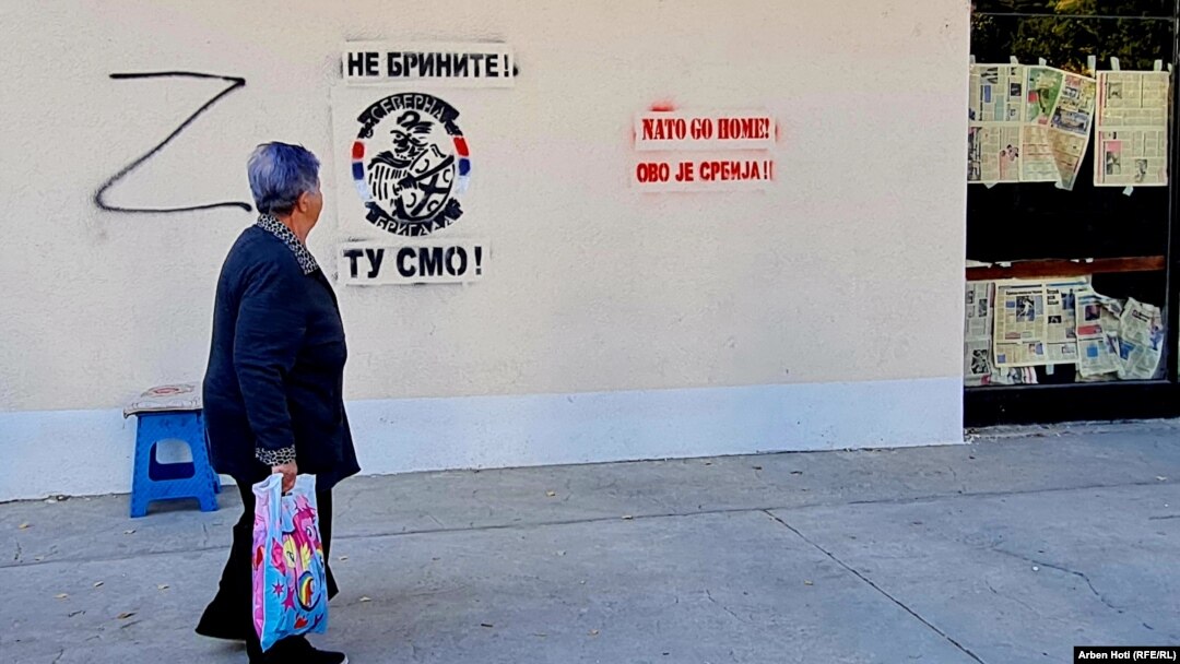 A woman walks past Northern Brigade graffiti in the divided city of North Mitrovica.