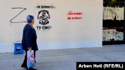 A woman walks past Northern Brigade graffiti in the divided city of North Mitrovica.