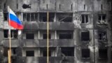 Російський прапор на тлі вигорілого – внаслідок бомбардувань і обстрілів російської армії –житлового будинку Маріуполя. 11 квітня 2022 року