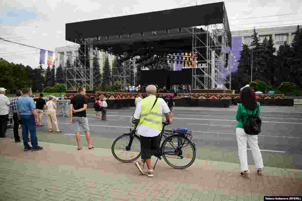 Un bărbat a venit pe bicicletă la concert. Pe scenă evoluează interpreți de muzică populară.