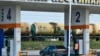 Заправка автомобиля на автозаправочной станции «Южной нефтяной компании». На дальнем плане - железнодорожные цистерны для транспортировки нефтепродуктов. Россия, Краснодар, 2020 год. Иллюстрационное фото 