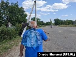 Житель села Афанасьевка Николаевской области несет емкости с питьевой водой, июнь 2023 года