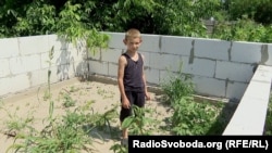 Павлик стоїть посеред фундаменту нового будинку. На цьому місці буде його кімната. Київська область, село Забуяння, 18 липня 2023 року