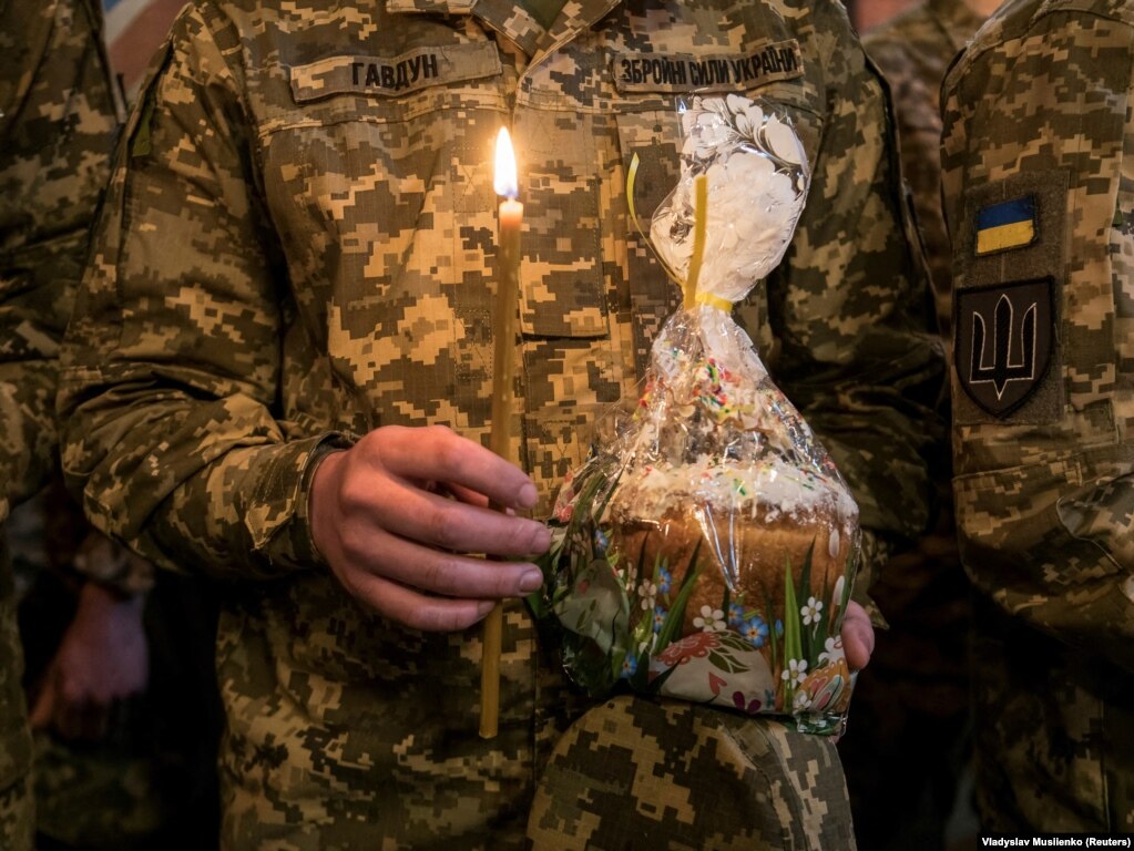 Një ushtar ukrainas mban në duar një qiri të ndezur dhe një tortë tradicionale të Pashkëve.