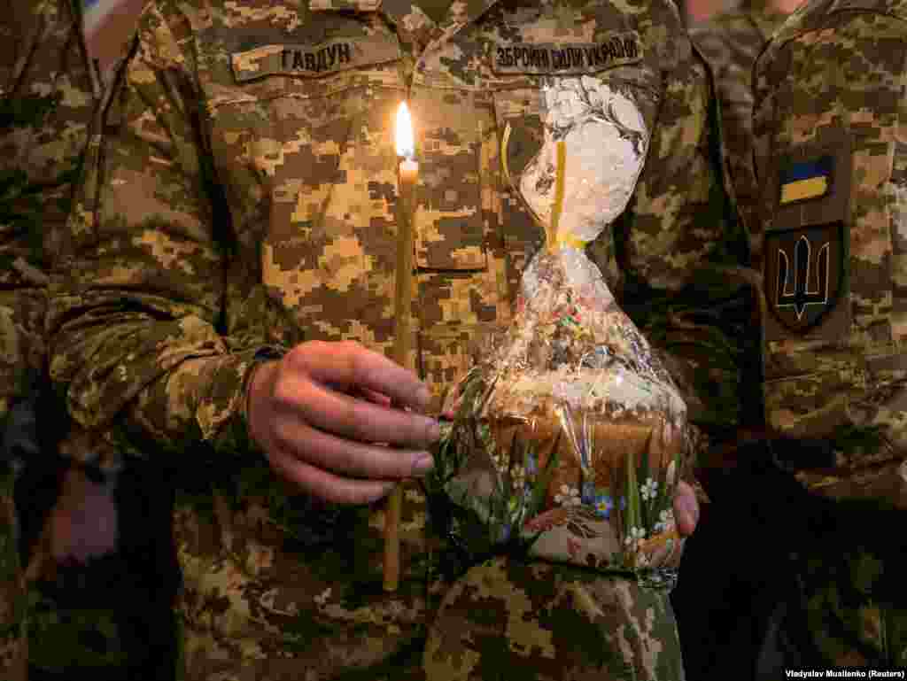 A Ukrainian soldier holds a lit candle and a traditional Easter cake that was blessed by a priest.