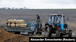 Рабочие едут в кузове трактора с гробами на кладбище в поселке Старый Крым под Мариуполем, контролируемом Россией. 4 февраля 2023 года.