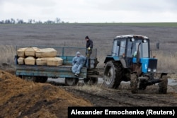 Munkások egy koporsókat szállító traktor hátulján ülnek a Mariupol melletti Sztarij Krim település temetőjében február 4-én