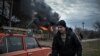 Një banor ukrainas pranë një ndërtese që po digjet pas granatimeve në rajonin e Donjeckut, më 15 mars 2023.