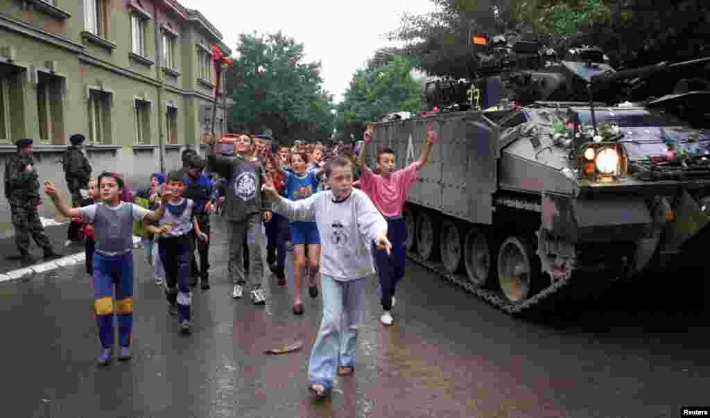 Copii aleargă pe lângă un tanc britanic după sosirea acestuia la Podujeva, 18 iunie 1999. Piața a fost extinsă cu copaci proaspăt plantați.