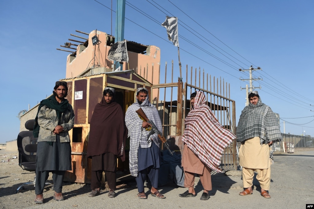 Taliban fighters stand guard at the entrance gate to an Afghan-Iran border crossing bridge in Zaranj.