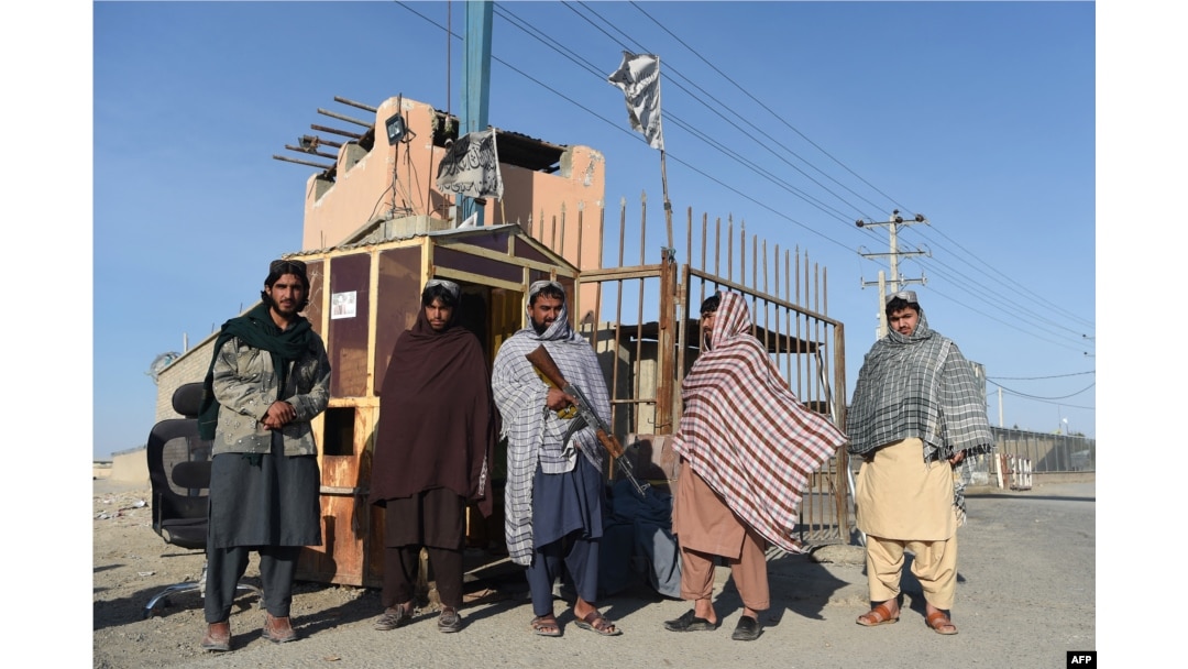 Taliban fighters stand guard at the entrance gate to an Afghan-Iran border crossing bridge in Zaranj.