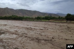 Residents stand next to a river covered with mud after flash floods in the village of Logariha in the Nahrin district of Baghlan Province on May 10.