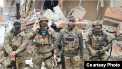 Аслан Очерхаджиев с бойцами батальона и украинскими военнослужащими на фоне разрушенного дома в Бахмуте