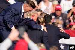 Momentul în care agenții Secret Service îl ridică pe Donald Trump (78 de ani) și îl evacuează de pe scenă. Alte câteva focuri de armă s-au auzit în jur în acele clipe, posibil din partea forțelor de ordine.