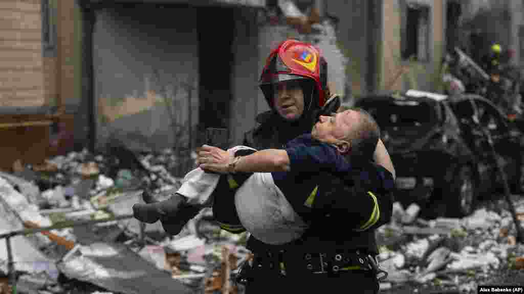 Egy tűzoltó a karjában visz ki egy sérültet a megrongálódott házból Kijevben