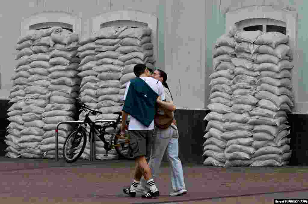 A couple kisses while walking by sandbags protecting the windows of the Palace of Children&#39;s Creativity in Kyiv.
