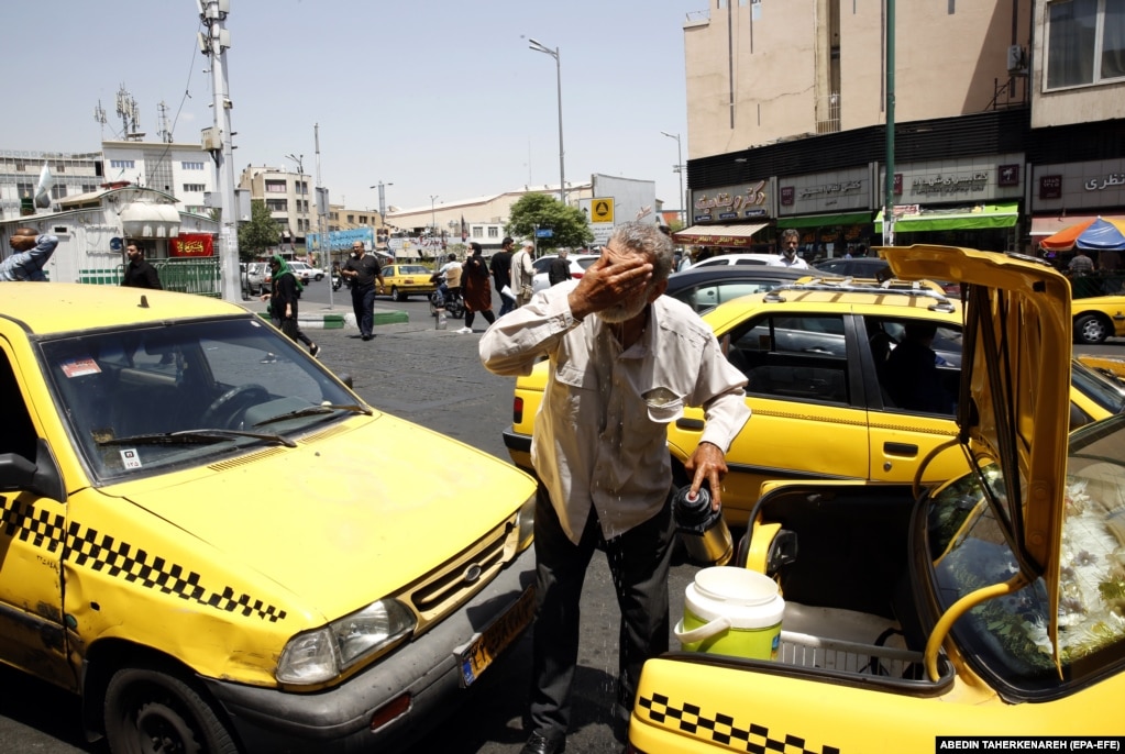 Un uomo a Teheran si spruzza la faccia con l'acqua dal retro del suo taxi.   