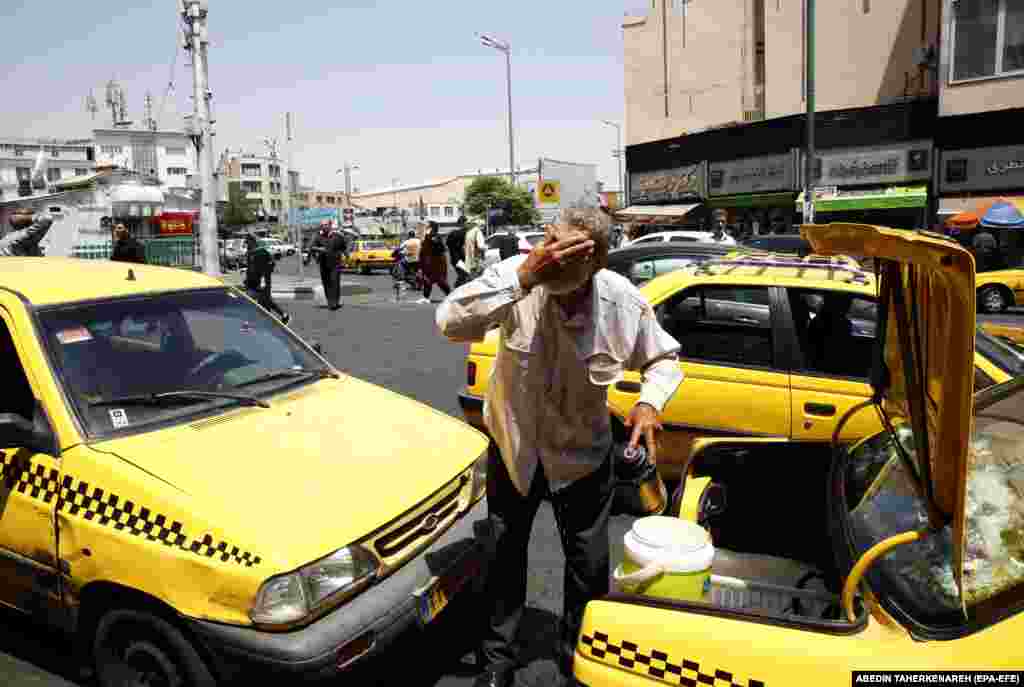 A man in Tehran splashes his face with water from the back of his taxi. &nbsp;