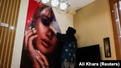 O cosmeticiană din Kabul, Afganistan, înlătură un poster dintr-un salon de înfrumusețare, pe 24 iulie 2023.