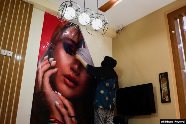 Un'estetista rimuove un poster da un salone di bellezza a Kabul, chiuso per ordine dei talebani.  24 luglio 2023