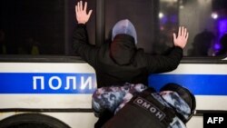 Полицай от силите за борба с безредиците претърсва задържан мъж по време на протест срещу съдебно решение, с което руският опозиционен лидер Алексей Навални е осъден на близо три години затвор, февруари 2021 г. 