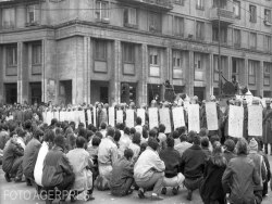 Manifestanți așezați pe asfalt, în fața șirurilor de scutieri din Piața Romană/bulevardul Gh. Magheru din București, 21 decembrie 1989. Mulți nu au supraviețuit măcelului care urma să aibă loc în noaptea care a urmat. Ultima noapte a comunismului în România.