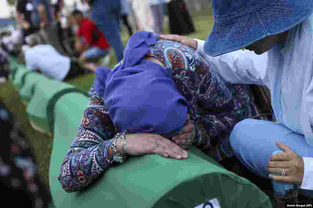 A Bosnian woman is comforted as she weeps over the coffin containing the remains of a relative.