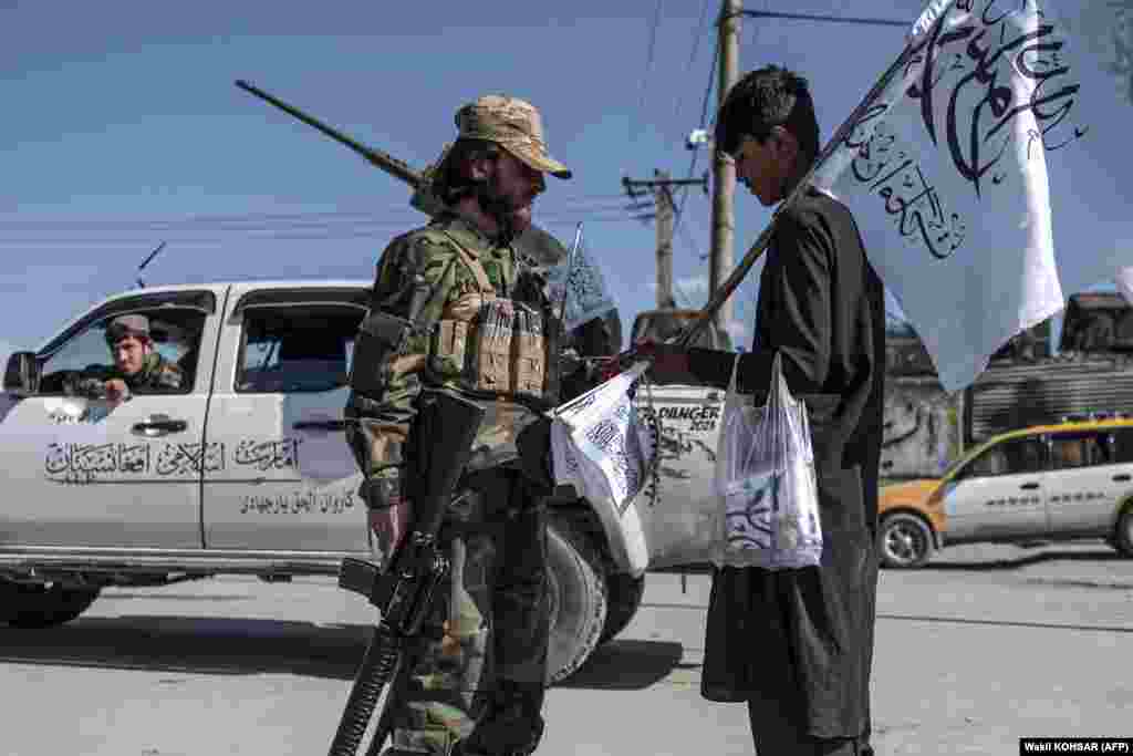 A Taliban fighter talks with a flag vendor outside the Eid Gah mosque in Kabul.
