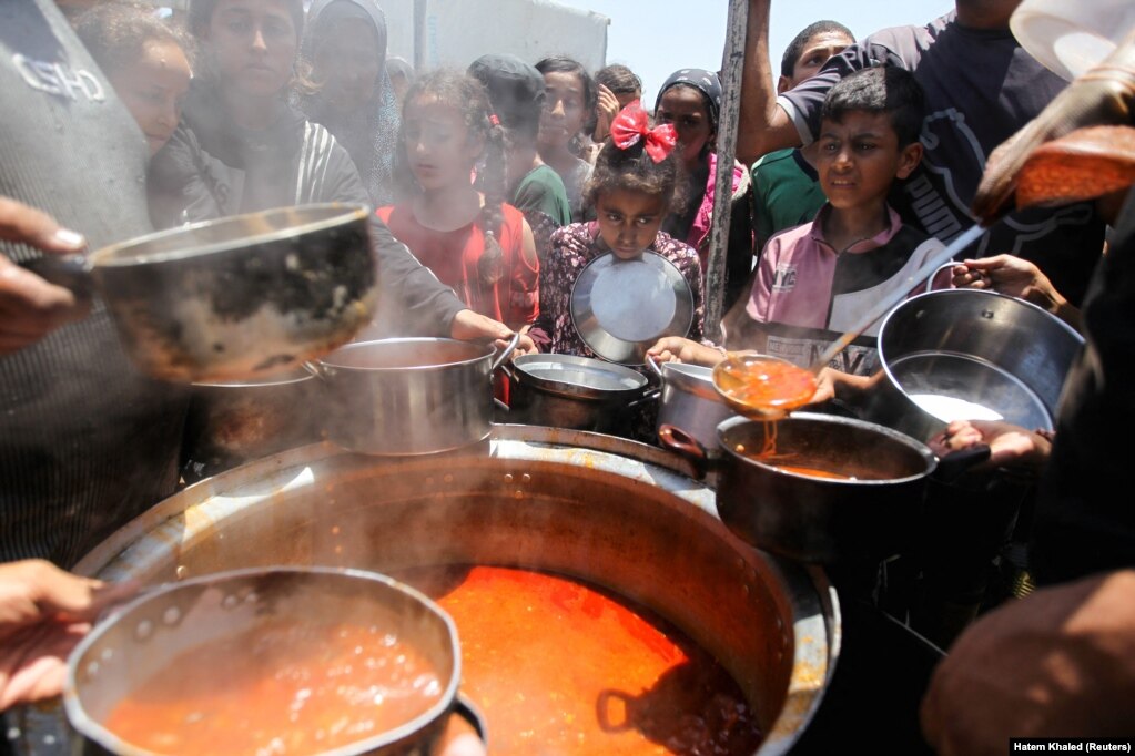 Turma e palestinezëve e mbledhur rreth një kazani me ushqim të gatuar nga një kuzhinë bamirësie.