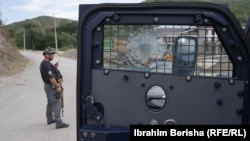 Xhami i një automjeti të blinduar të Policisë së Kosovës shihet i dëmtuar nga të shtënat me armë zjarri, teksa një polic qëndron duke vëzhguar, në Banjskë të Zveçanit, më 27 shtator 2023, tri ditë pas një sulmi ndaj Policisë atje nga një grup serbësh të armatosur.