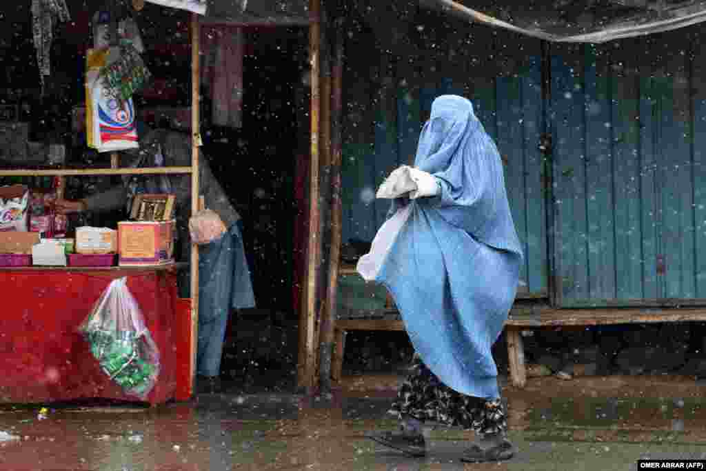 An Afghan woman in a burqa walks along a street as snow falls in Fayzabad, Badakhshan Province.