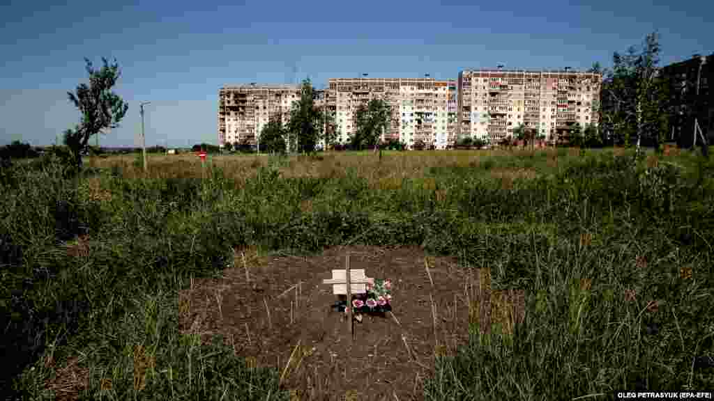 The impromptu grave of a local resident lies in a field near damaged apartment buildings.&nbsp; The proximity of the town to the front line has resulted in the deaths of&nbsp;some 60 citizens,&nbsp;including three children.