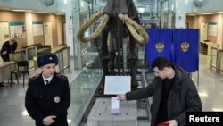 Полицай наблюдава мъж, който гласува в избирателна секция в Новосибирския държавен университет, 17 март 2024 г.