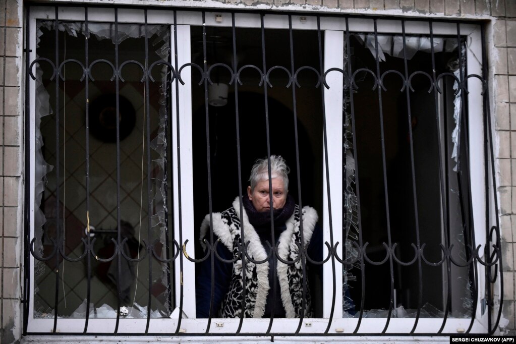 Una donna osserva la scena dal suo appartamento le cui finestre sono andate in frantumi durante l'attacco.  Sia Mosca che Kiev negano di aver preso di mira i civili nella guerra durata quasi 22 mesi che la Russia ha lanciato contro il suo vicino nel febbraio 2022.