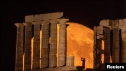 Osoba fotografiše dok se pun mjesec poznat kao "Buck Moon" diže iza Posejdonovog hrama, na rtu Sounion, blizu Atine, Grčka, 3. jula 2023. 