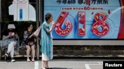 Ljudi čekaju autobus pored reklamnog postera za festival šopinga '618' u Pekingu, 12. juni 2023. 