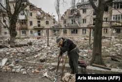 An elderly man collects wood from debris in front of a destroyed apartment building in Avdiyivka in March 2023.