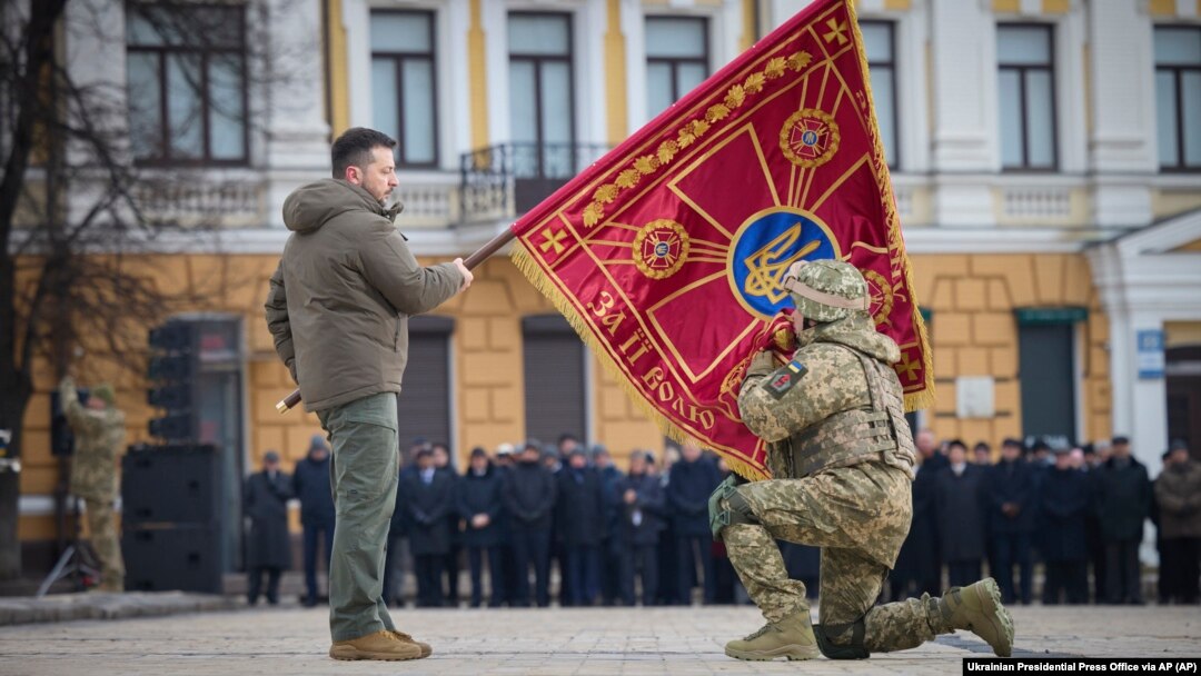 A Ukrainian Army officer kisses the flag of a military unit held by Ukrainian President Volodymyr Zelenskiy during a ceremony marking the anniversary of Russian's invasion, on February 24. 